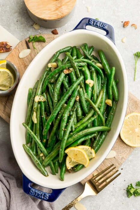 Top view of roasted green beans with garlic in a oval blue casserole dish on a wooden cutting board