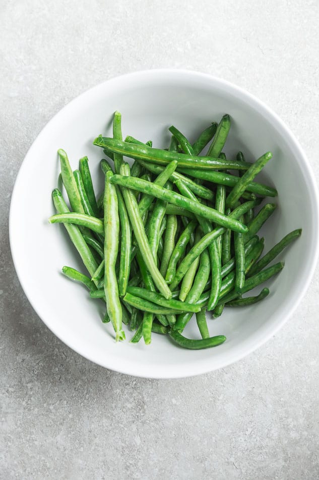 A white bowl full of raw green beans