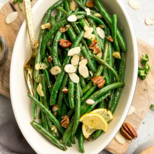 Top view of roasted green beans with slivered almonds and pecans in a oval blue casserole dish on a wooden cutting board