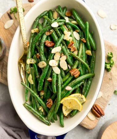 Top view of roasted green beans with slivered almonds and pecans in a oval blue casserole dish on a wooden cutting board