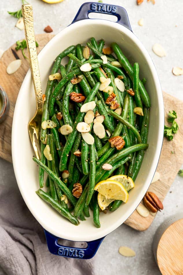 Top view of roasted green beans with slivered almonds and pecans in a oval blue casserole dish on a wooden cutting board