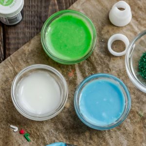 Top view of royal icing in blue, green and white for sugar cookies on a wooden board