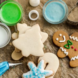 Top view of a batch of decorated sugar cookies and a gingerbread man cookie on a wooden board surrounded by icing.