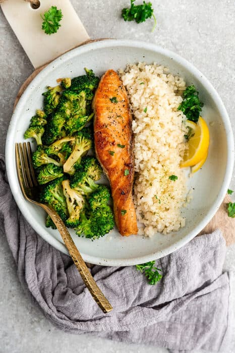 Top view image of keto cauliflower rice in a white bowl served with salmon and broccoli