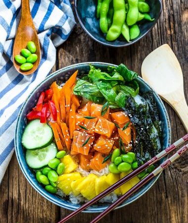 Top view of salmon poke bowl with chopsticks on a wooden background