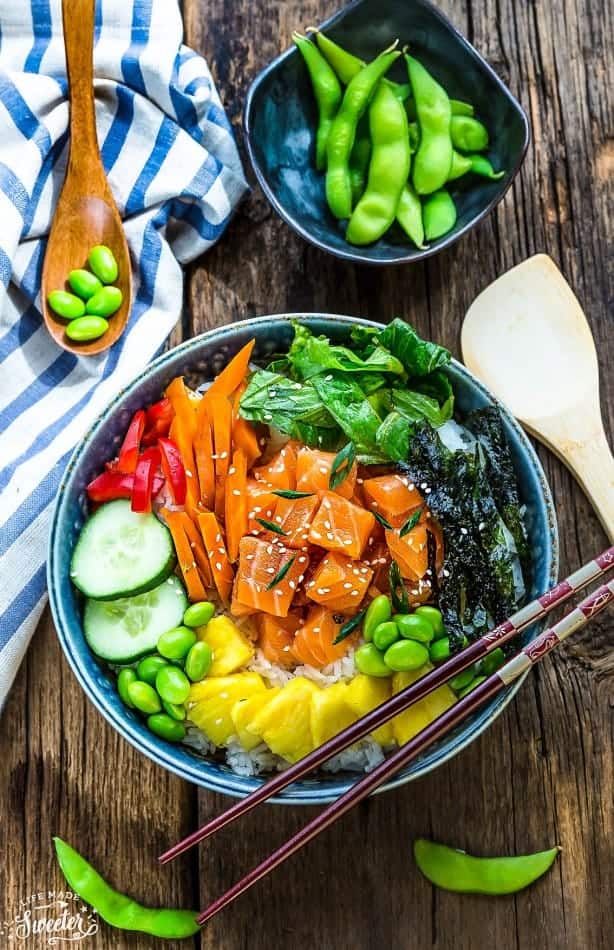 An overhead shot of a salmon poke bowl beside a dish of edamame