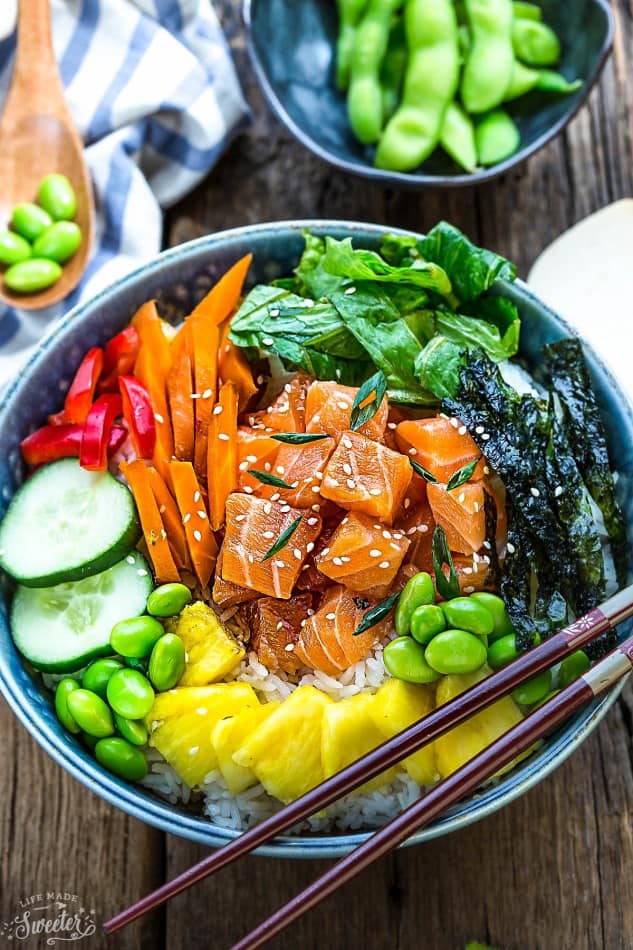 A salmon poke bowl with a pair of wooden chopsticks resting on the rim of the bowl