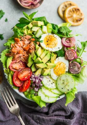 Top view of fresh salmon salad in a white bowl on a light grey background with a dark grey napkin and fork