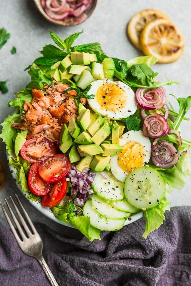 Top view of fresh salmon salad in a white bowl on a light grey background with a dark grey napkin and fork