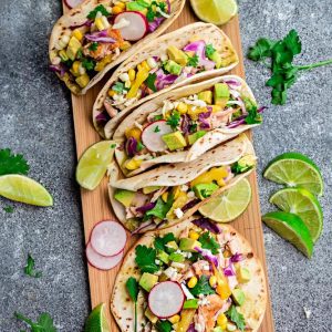 Easy Salmon Tacos - packed with flavor and come together in 30 minutes - perfect for your next Taco Tuesday! Topped with lettuce, red cabbage, corn, pineapple and avocado cream