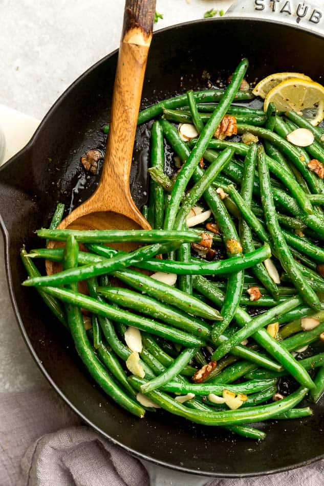 Fresh green beans sauteed in black pan with wooden spoon.