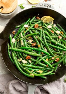 Close-up top view of sauteed green beans in a grey cast iron skillet on a grey background