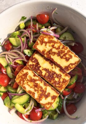 Three rectangle slabs of seared Halloumi cheese over a bed of mixed salad greens in a white bowl