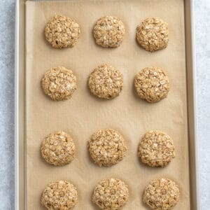 Top view of 12 tahini cookies on a baking sheet on a grey background