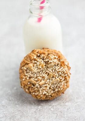 Top view of one sesame tahini cookie leaning on a milk jug on a grey background