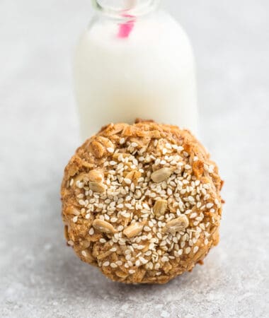 Top view of one sesame tahini cookie leaning on a milk jug on a grey background