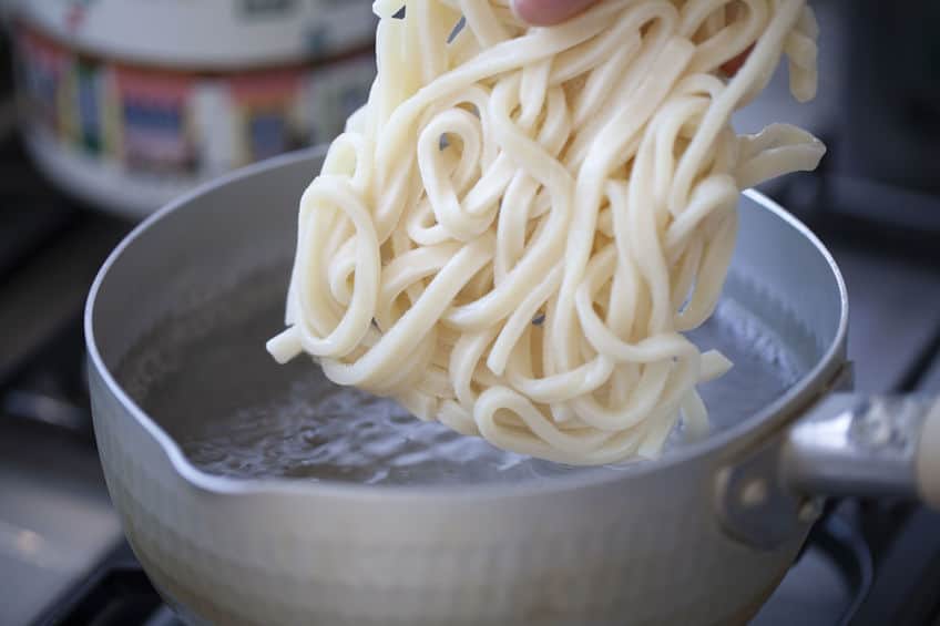 Side view of uncooked shanghai noodles over a pot of boiling water