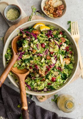 Top view of shaved Brussels Sprouts Salad in a white bowl with two wooden spoons on a wooden cutting board