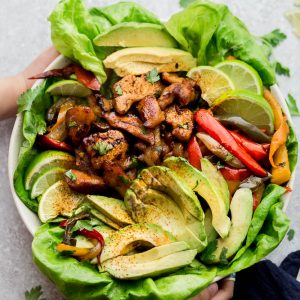 Sheet pan chicken fajitas in a bowl with a bed of lettuce and fresh avocado slices