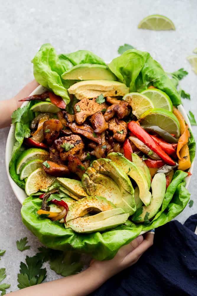 Sheet pan chicken fajitas in a bowl with a bed of lettuce and fresh avocado slices