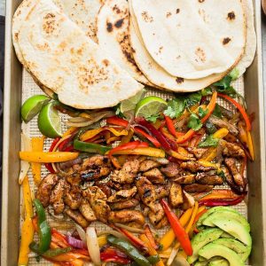 Warm tortillas on a sheet pan with roasted chicken, bell peppers and red onions
