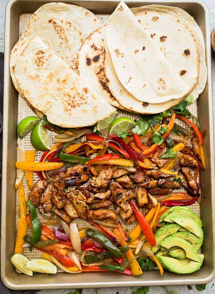 Warm tortillas on a sheet pan with roasted chicken, bell peppers and red onions