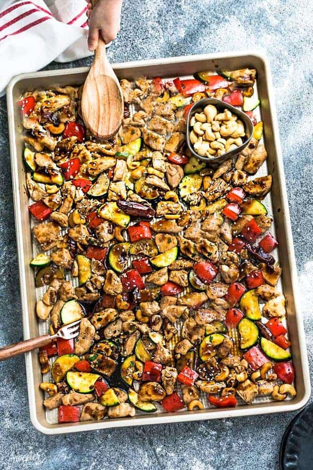Top view of Sheet Pan Kung Pao Chicken with a wooden spoon and a cup of cashews