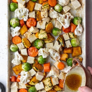 Uncooked Brussels sprouts, cauliflower, carrots, onions and tofu in a baking sheet