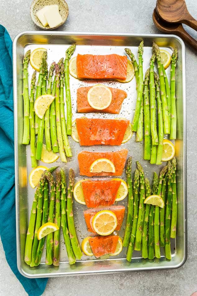 Top view of raw salmon filets on a sheet pan with asparagus and lemon