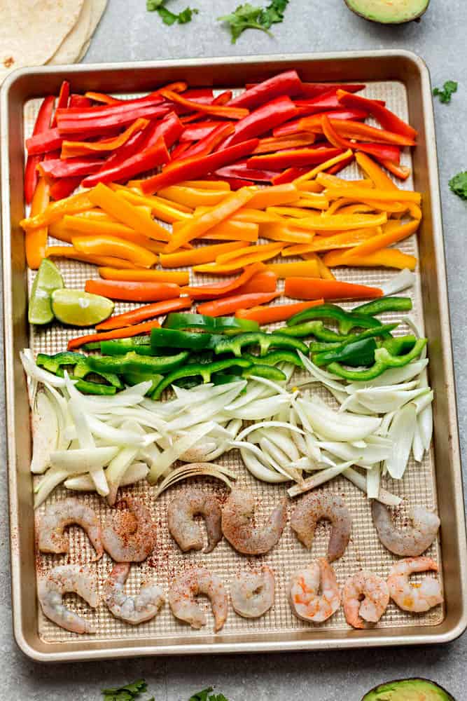 uncooked bell peppers, onions, and shrimp on a sheet pan for a sheet pan fajitas dinner