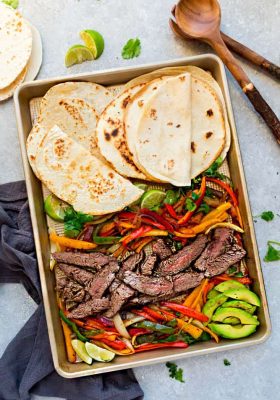 Top view of Sheet Pan Steak Fajitas on a baking sheet with avocado, lime and Whole30 tortillas
