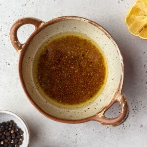Coconut aminos, lemon juice, oil, and mustard in beige bowl