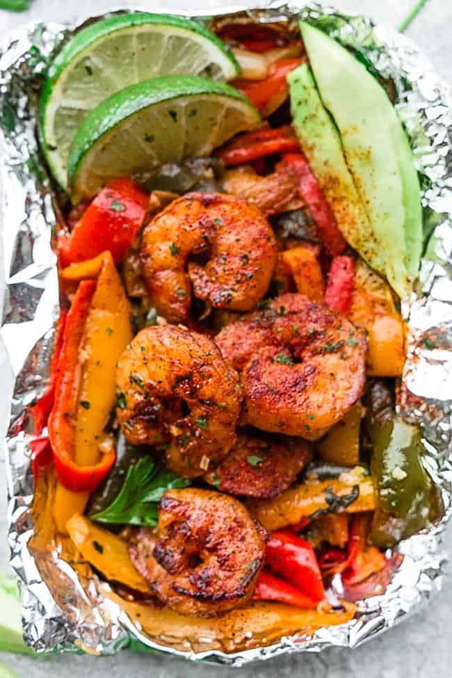 Close up view of shrimp fajita foil packets with lime and colorful vegetables.