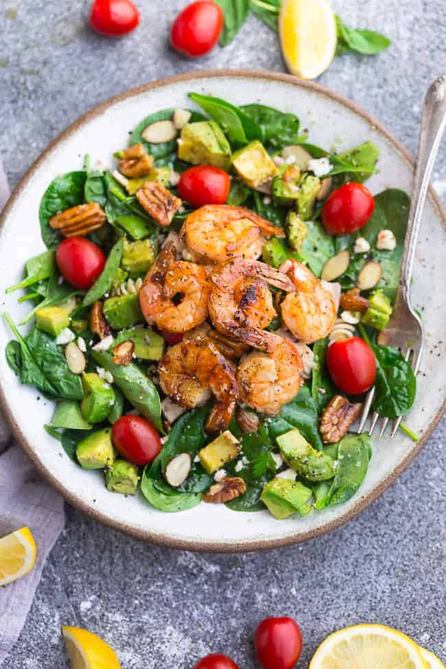 Top view of shrimp salad on a white plate on a grey background with a fork