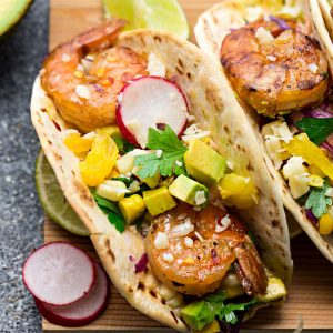 Healthy Shrimp Tacos - made with a delicious spicy seasoning and come together in 30 minutes – perfect for your next Taco Tuesday! Best of all, instructions to make this on the grill or stove and packed with avocado, lettuce, red cabbage, pineapple and avocado cream.