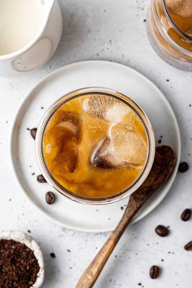 An overhead shot of brewed coffee in a glass with a wooden spoon beside it