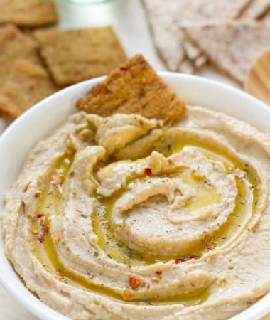 A bowl of homemade hummus in a white bowl with a cracker
