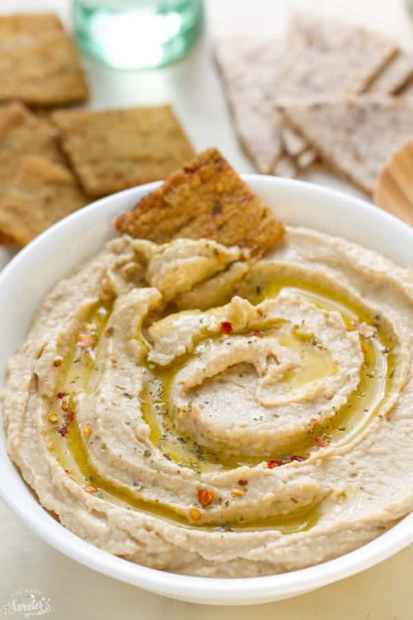 A bowl of homemade hummus in a white bowl with a cracker