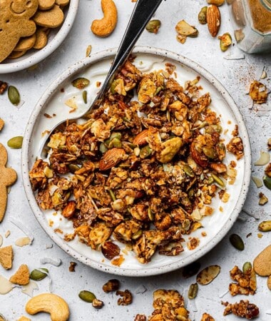 Top view of a white bowl of gingerbread granola in yogurt with a spoon