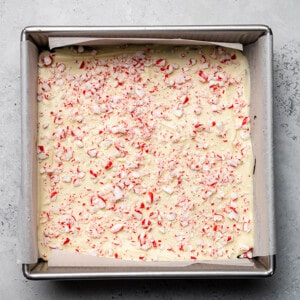 Top view of melted white chocolate with chopped candy canes in a square baking pan
