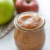 A small jar of Slow Cooker Apple Butter in front of a few apples