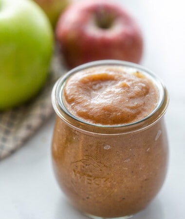 A small jar of Slow Cooker Apple Butter in front of a few apples