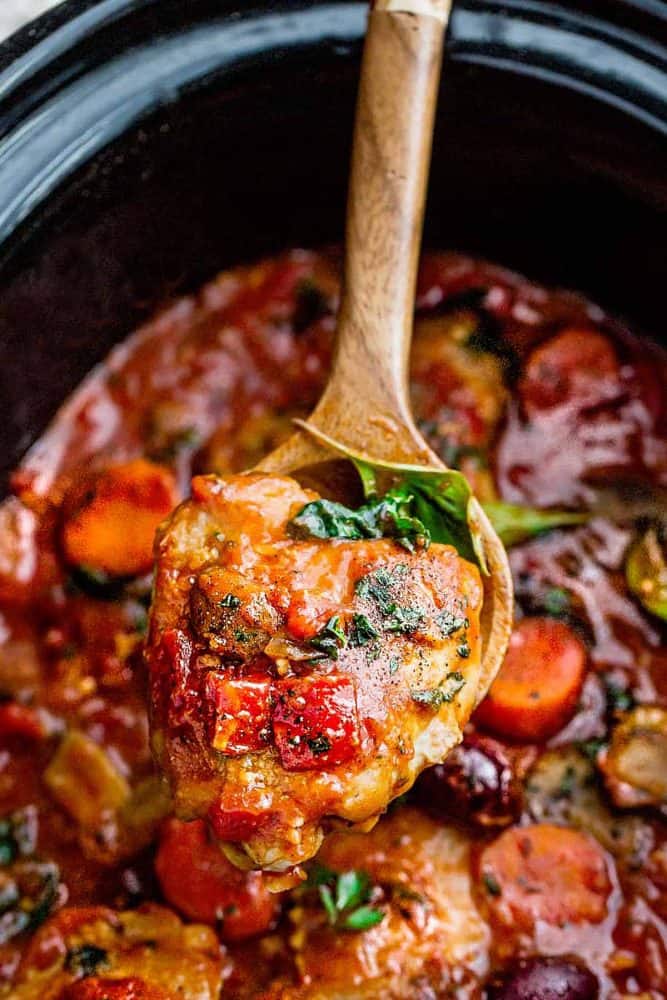 wooden spoon holding a serving of chicken cacciatore in a slow cooker