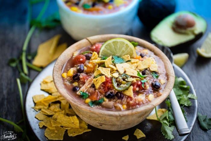 A bowl of Slow Cooker Chicken Enchilada Quinoa Soup topped with crushed tortilla chips and a lime wedge