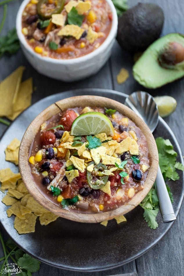 A bowl of Slow Cooker Chicken Enchilada Quinoa Soup topped with tortilla chip crumbs and a lime wedge