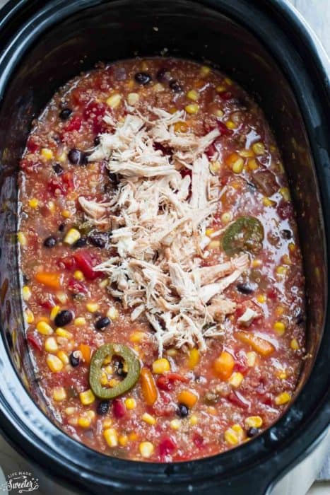 Overhead view of Slow Cooker Chicken Enchilada Quinoa Soup in a slow cooker topped with shredded chicken