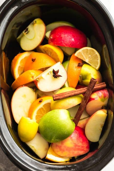 Top view of apples, oranges, cinnamon and cloves in a crockpot