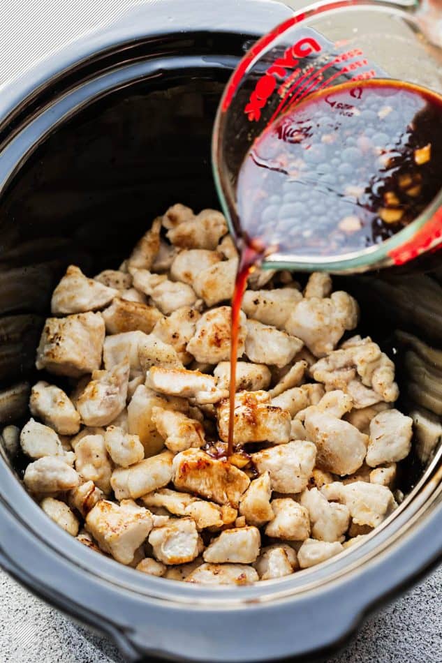 pouring a sweet and spicy Asian sauce over diced chicken pieces to make General Tsao's Chicken