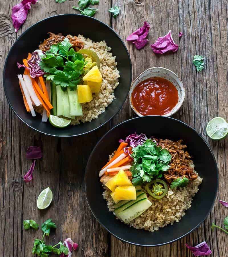 Top view of two Slow Cooker Honey Sriracha Pulled Pork Quinoa Bowls with colorful vegetables and a bowl of Sriracha sauce