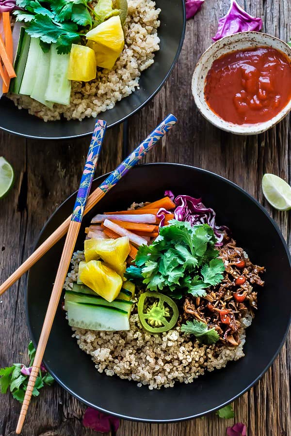 Top view of two Slow Cooker Honey Sriracha Pulled Pork Quinoa Bowls with colorful vegetables and a bowl of Sriracha sauce